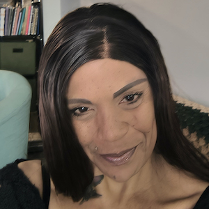 A woman with light brown skin and warm dark eyes smiles.